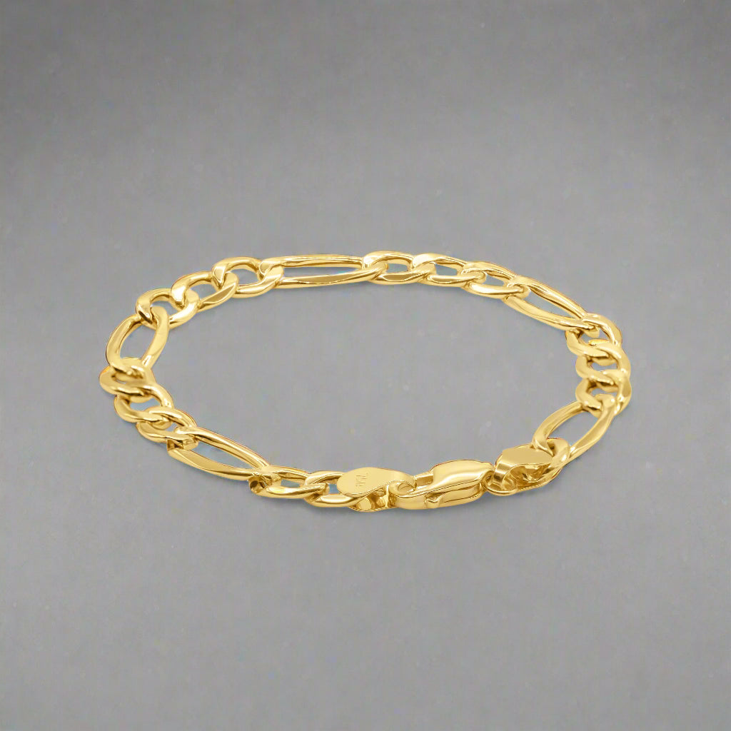 A gold Figaro chain bracelet with a classic and elegant design. The bracelet features a distinctive pattern of interlocking links, alternating between one elongated oval link and three smaller round links, characteristic of the Figaro style. Each link is polished to a high shine, enhancing the bracelet's luxurious appearance. The bracelet is secured with a sturdy lobster clasp, ensuring durability and ease of use. Its smooth surface and intricate link pattern reflect exceptional craftsmanship. 