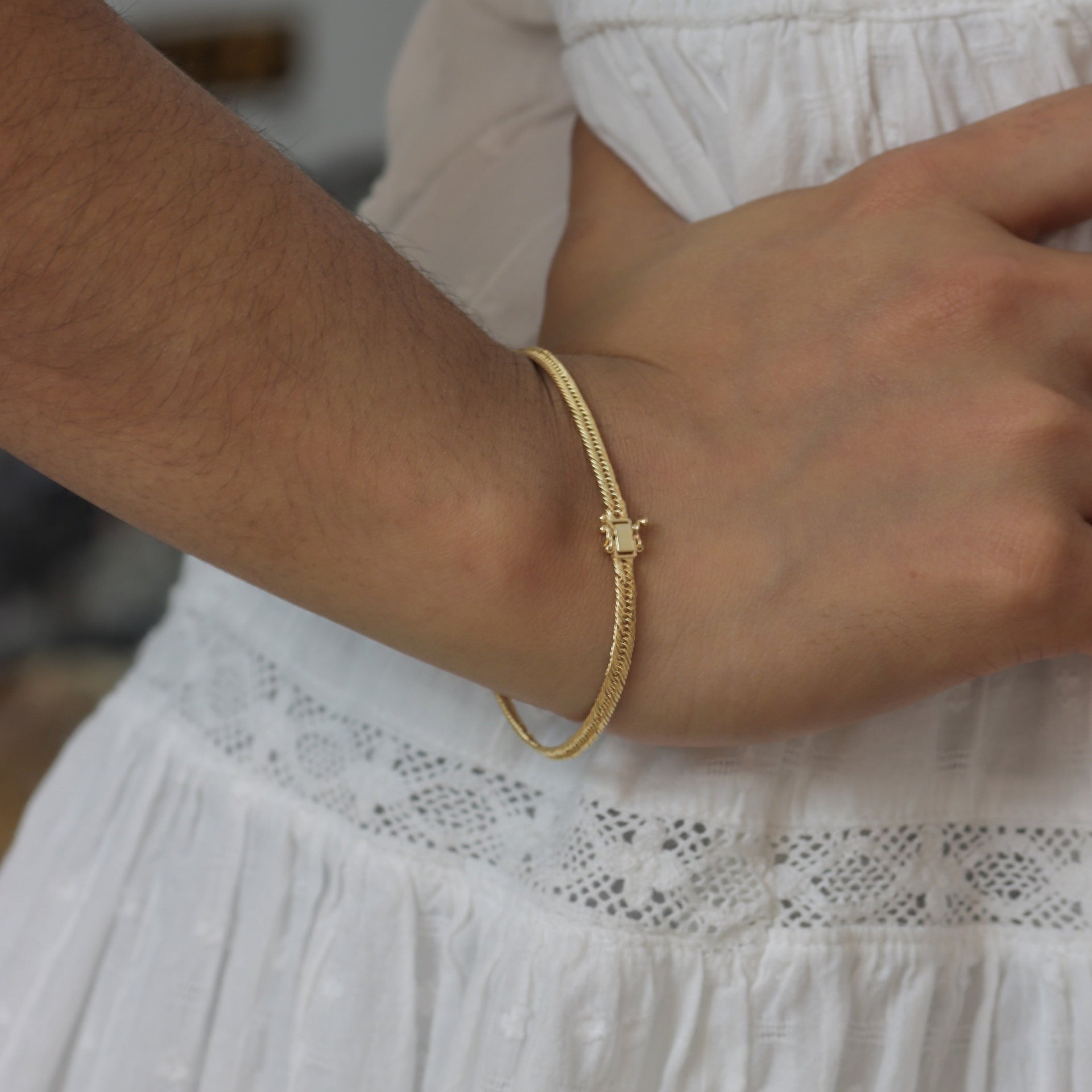 Gold bracelet on a wrist with a white dress in the background