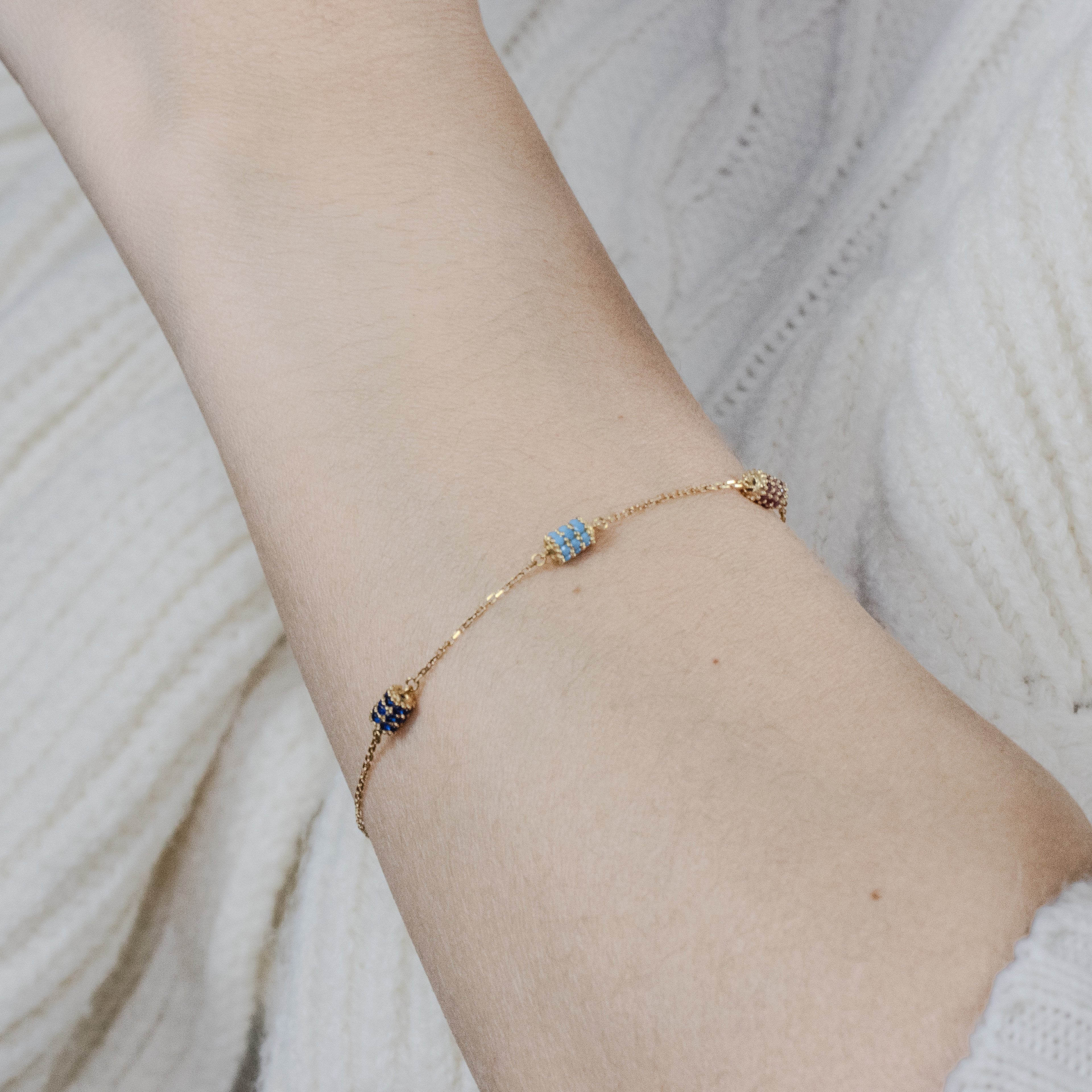 Chain bracelet adorned with 3 barrel charms  in dark blue, light blue and maroon worn around a woman's wrist