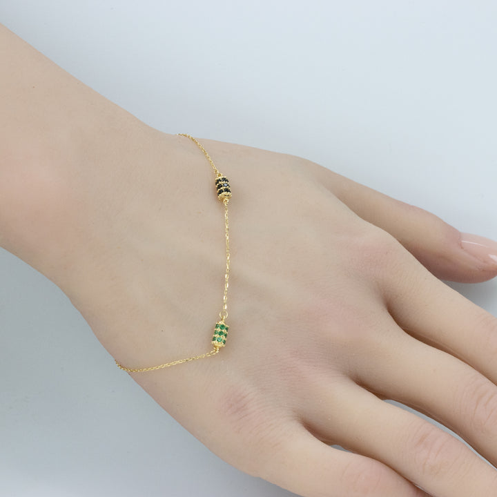 Wrist adorned with a double-barrel chain bracelet, featuring one green and one black barrel charm