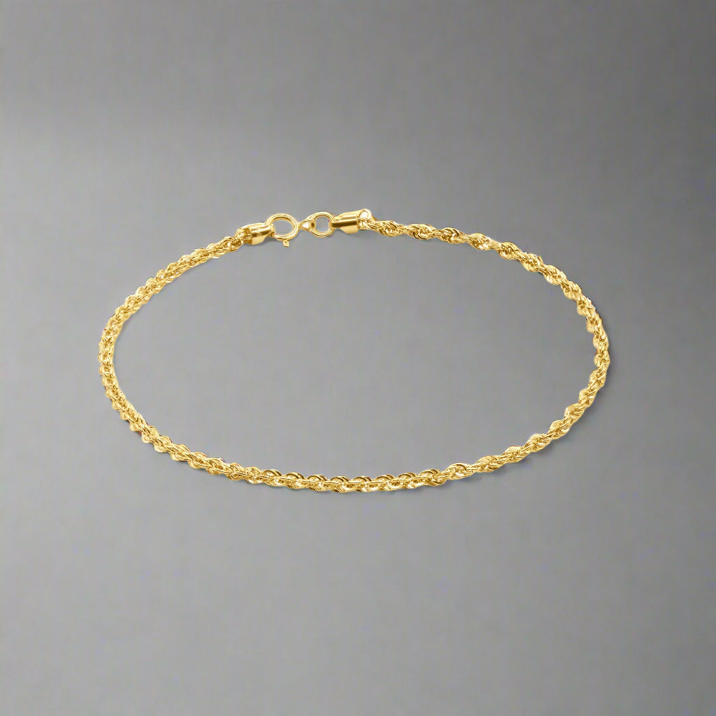 A gold wheat chain bracelet with a delicate and intricate design. The bracelet features tightly interwoven links, forming a braided pattern that is characteristic of the wheat chain style. The polished finish of the links gives the bracelet a luxurious shine and enhances its texture. It is equipped with a secure spring ring clasp at one end and a small jump ring at the other, ensuring both functionality and a seamless appearance. The bracelet's slender and elegant design makes it suitable for layering 