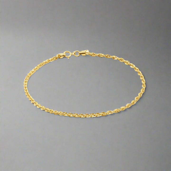 A gold wheat chain bracelet with a delicate and intricate design. The bracelet features tightly interwoven links, forming a braided pattern that is characteristic of the wheat chain style. The polished finish of the links gives the bracelet a luxurious shine and enhances its texture. It is equipped with a secure spring ring clasp at one end and a small jump ring at the other, ensuring both functionality and a seamless appearance. The bracelet's slender and elegant design makes it suitable for layering 