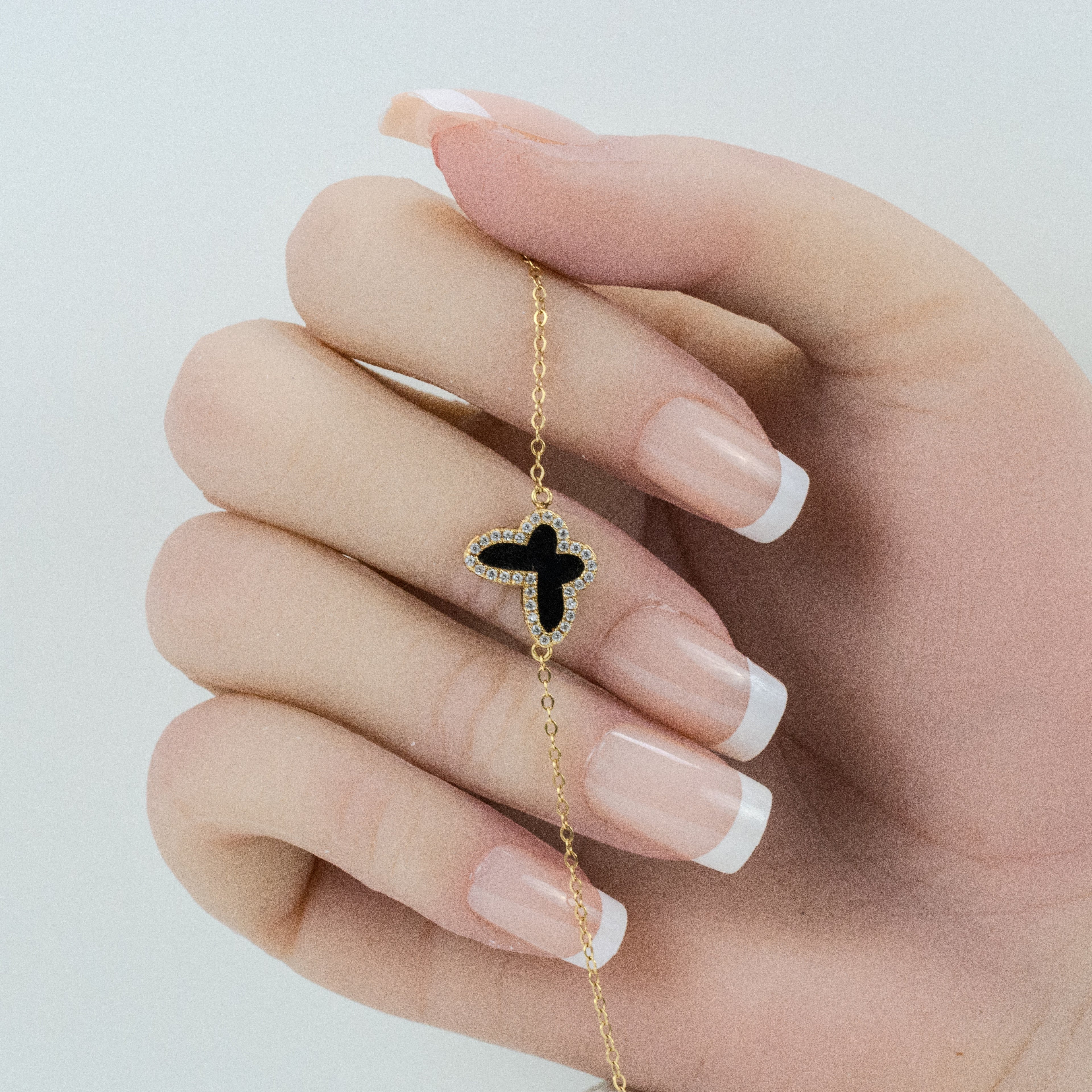 Hand displaying the chain bracelet, highlighting the front view of the black butterfly charm with diamonds accentuating its border