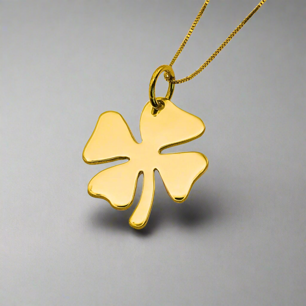 A close-up image of a gold clover leaf pendant hanging from a delicate gold chain. The pendant is polished to a high shine, showcasing its smooth surface and elegant design. The four-leaf clover shape symbolizes luck and prosperity, making this piece both a stylish accessory and a meaningful charm.